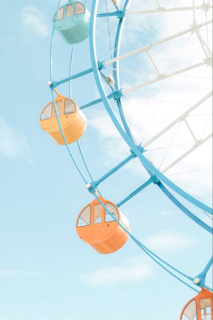 A ferris wheel with orange and blue cars against a light blue sky