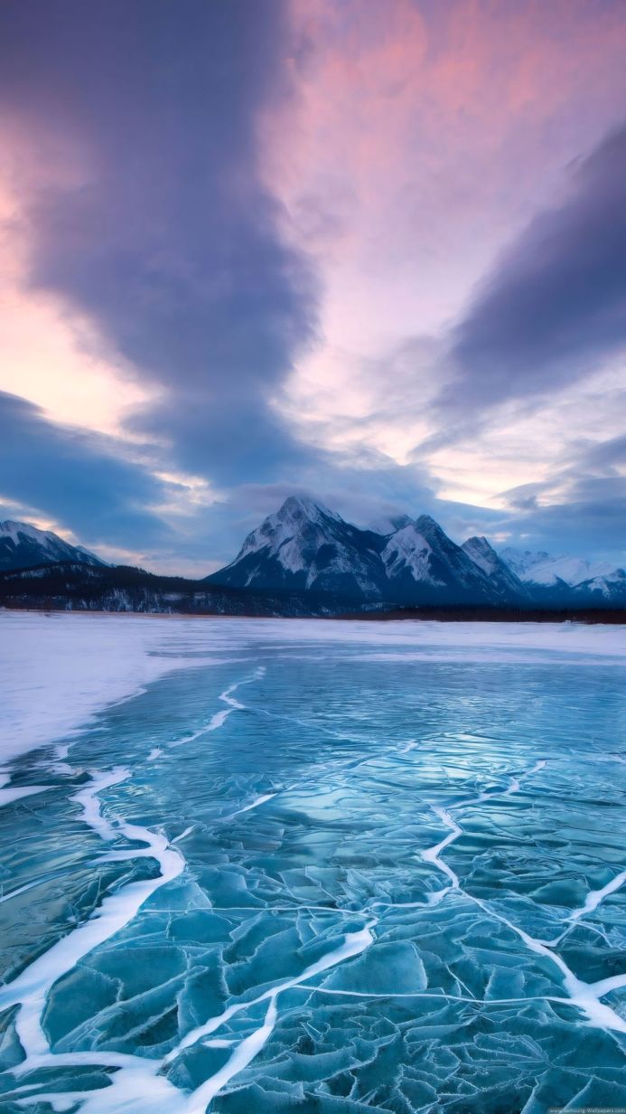 Cracked ice on a frozen lake with mountains in the background under a cloudy sky