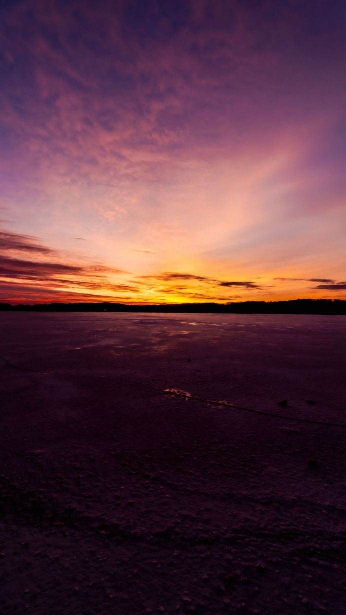 Colorful sunset over a frozen lake with a silhouette of trees in the background