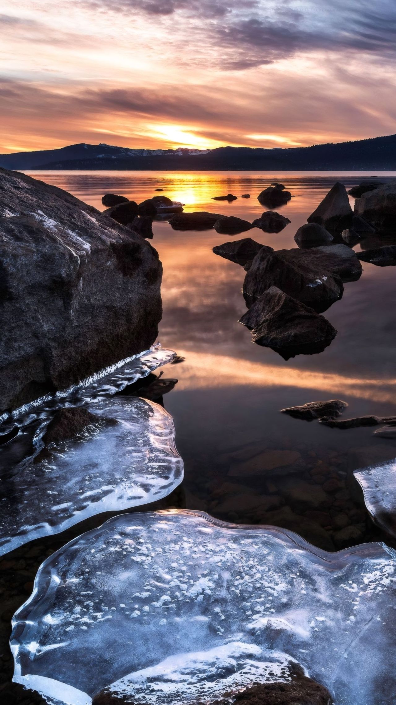 Winter sunset over lake with rocks and ice