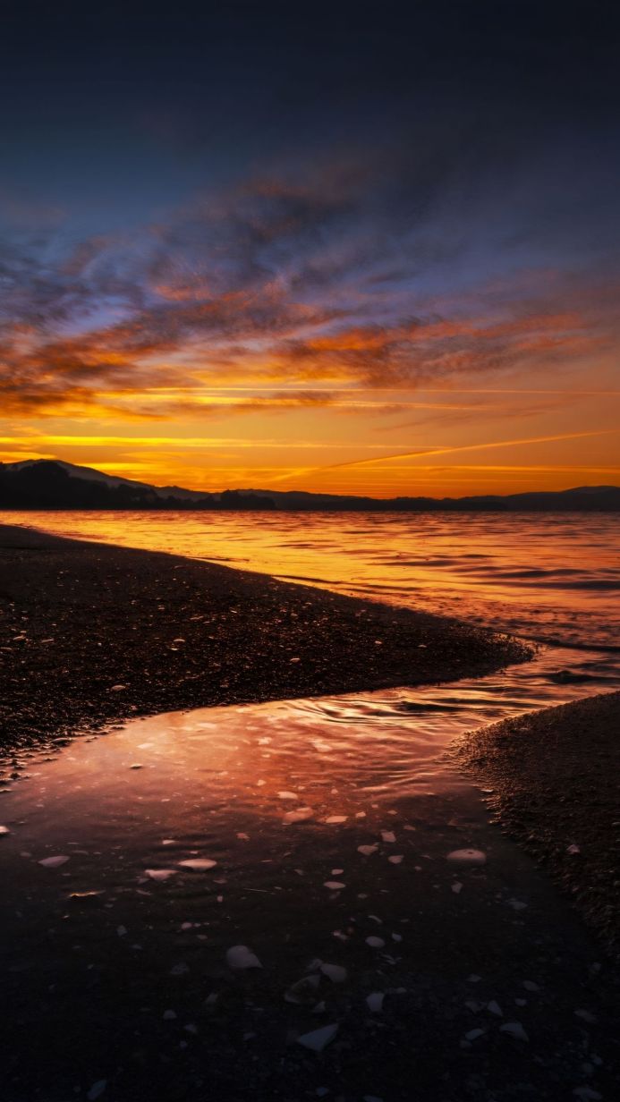 Lake reflecting the colorful sunset sky with mountains in the background