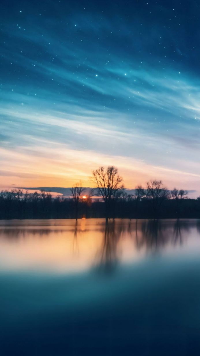 Lake at sunset reflecting bare trees under a starry sky