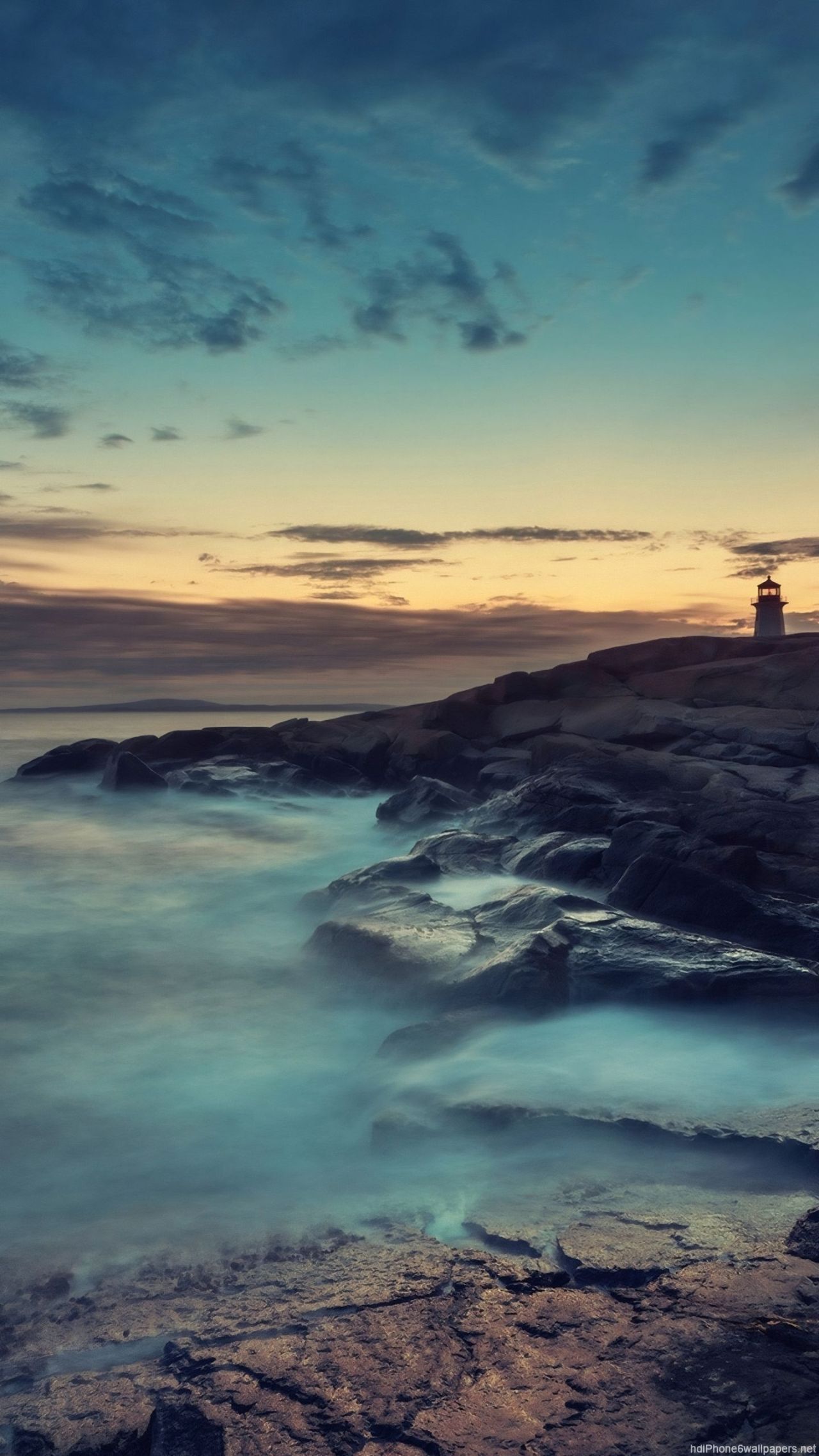 Lighthouse on rocky coast at sunset with misty water
