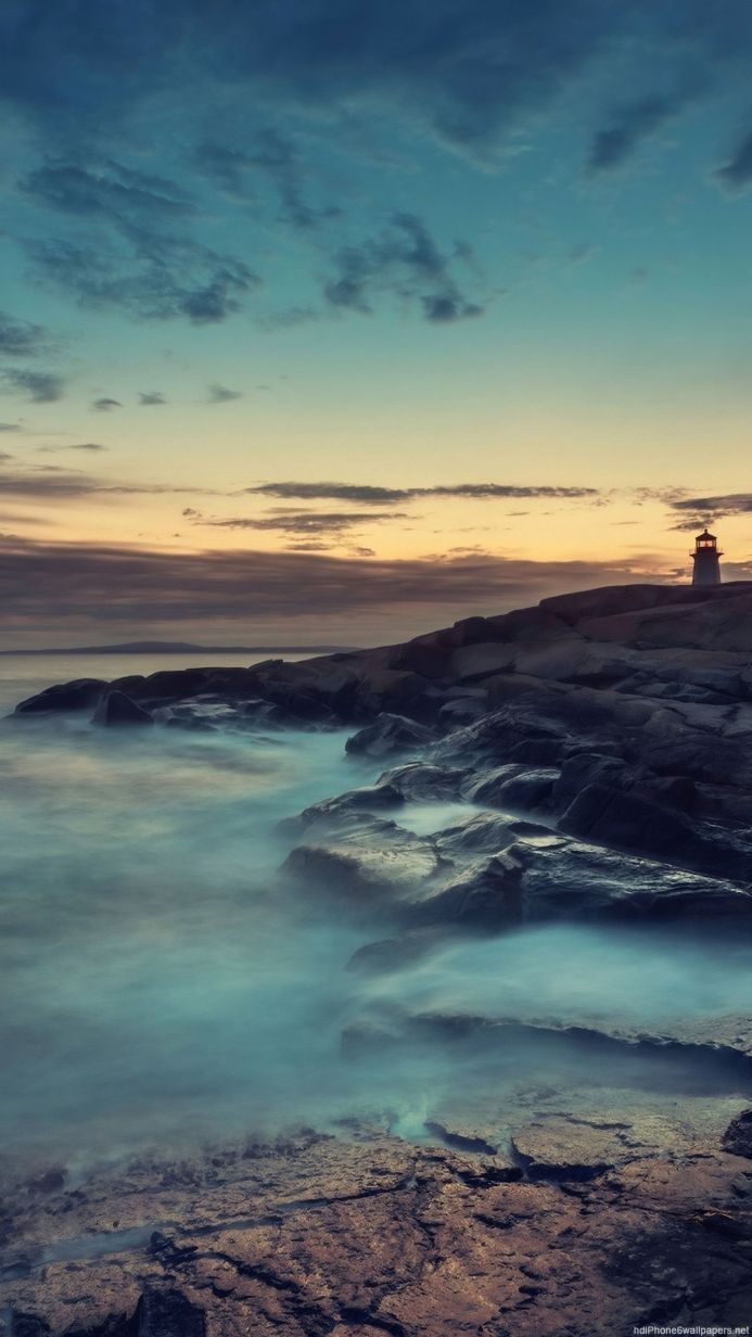 A lighthouse on rocks by the sea at sunset with long exposure water