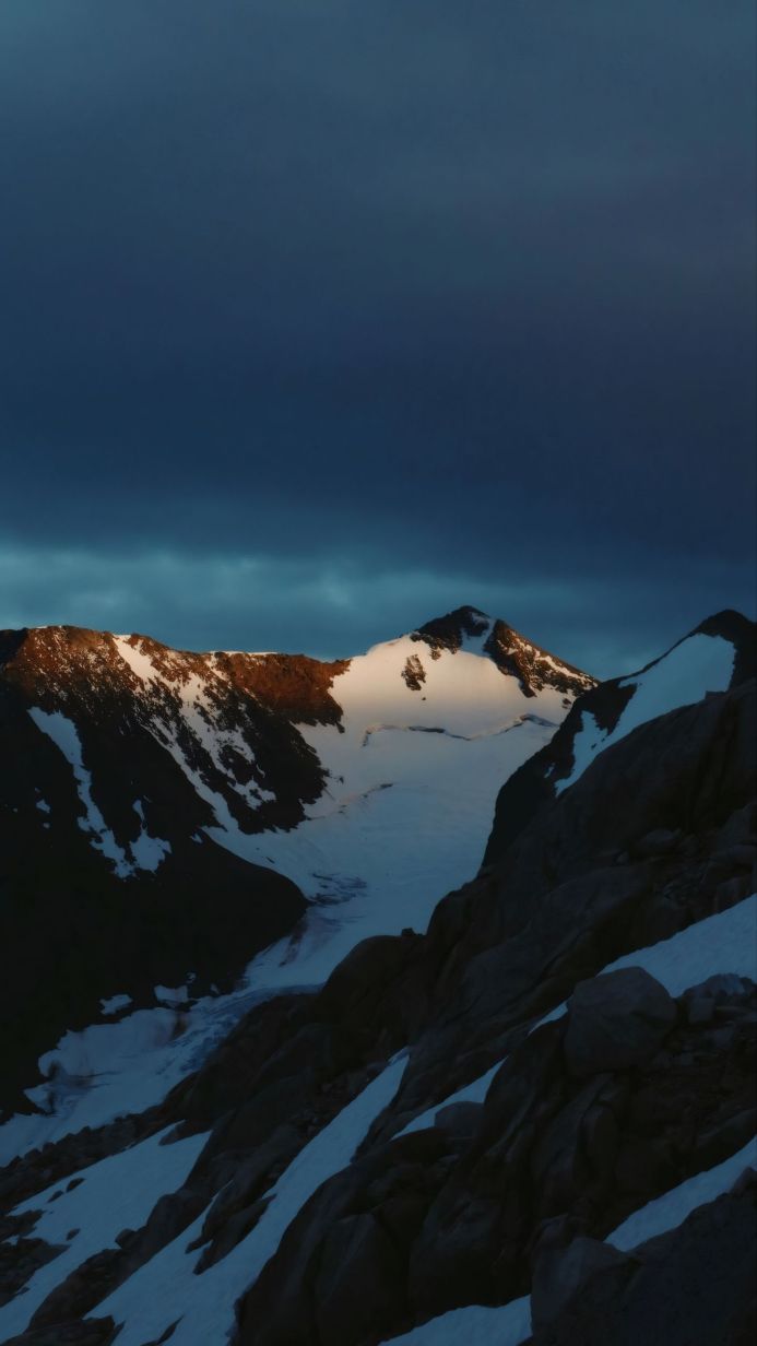 Mountain range with snow and glacier under a dark, cloudy sky