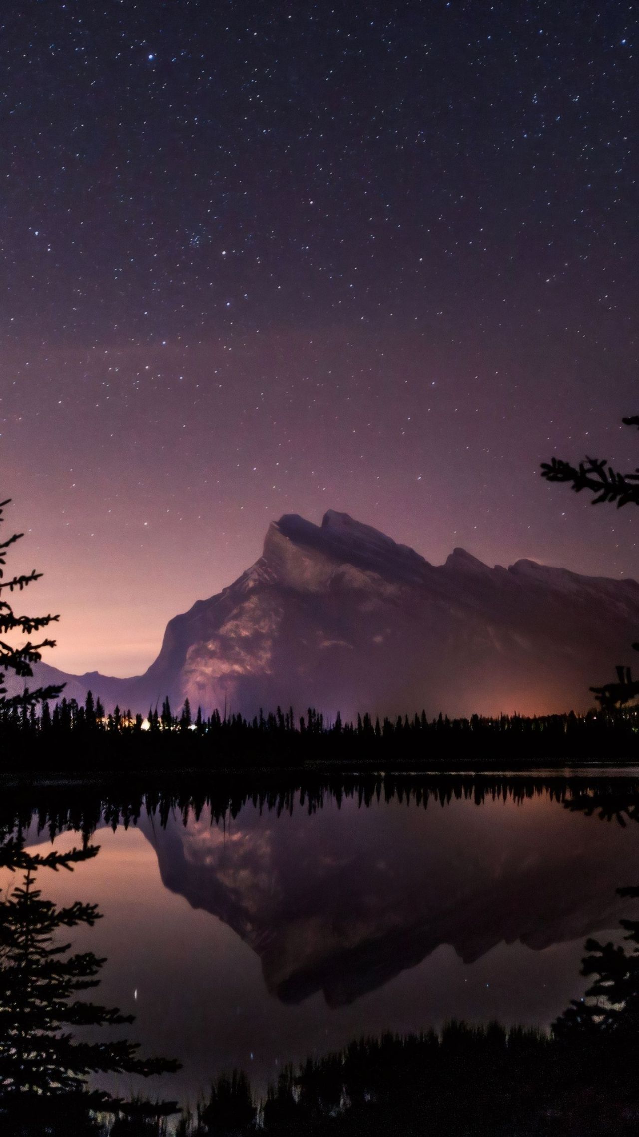 Starry night sky over mountain reflected in lake
