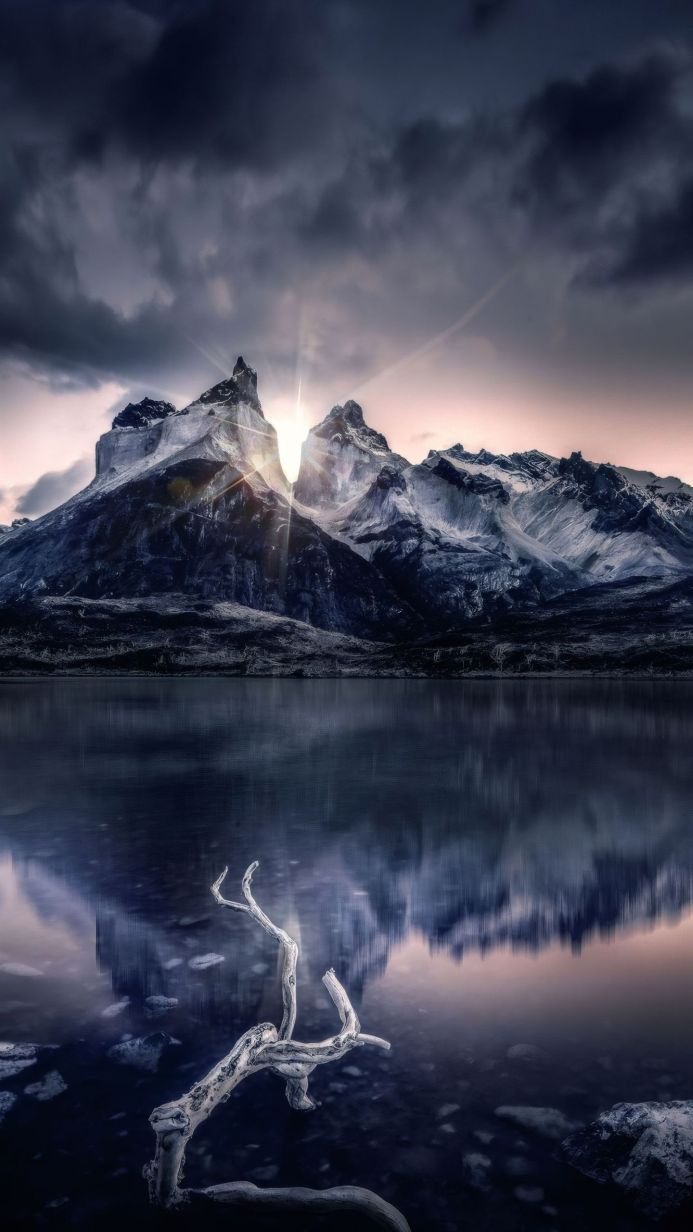 Mountains reflected in a lake with a branch in the foreground, dramatic sky