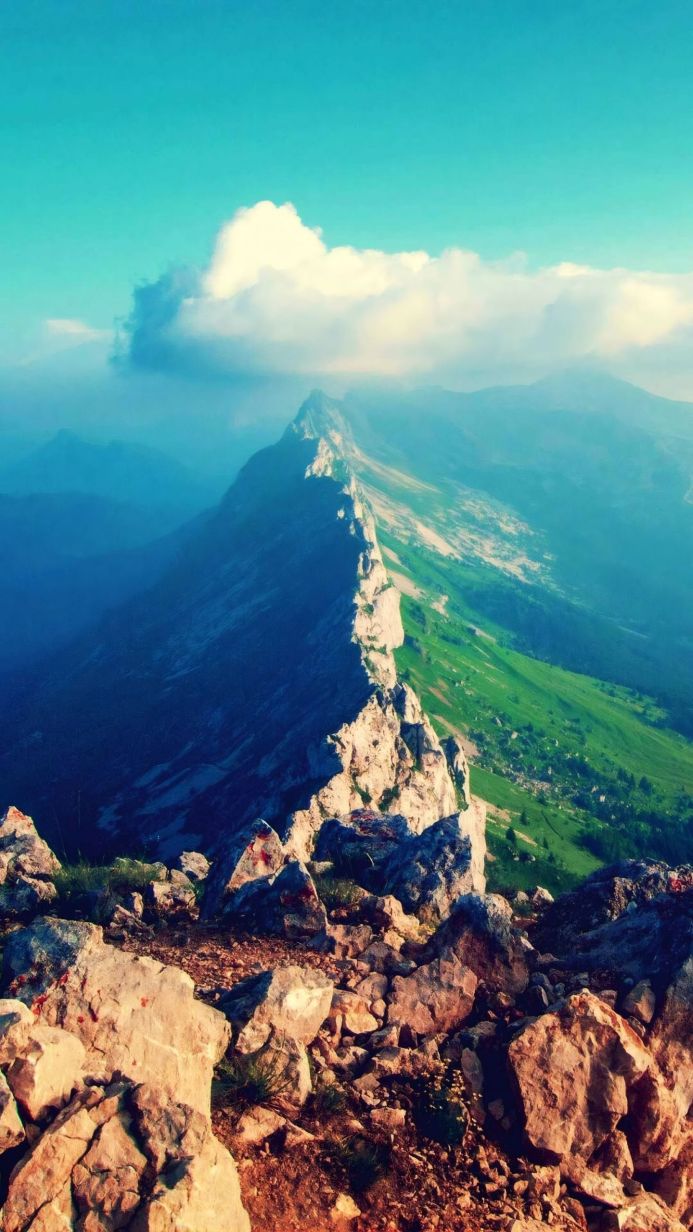 Panoramic view of a mountain range with green meadows and a rocky peak under a cloudy sky