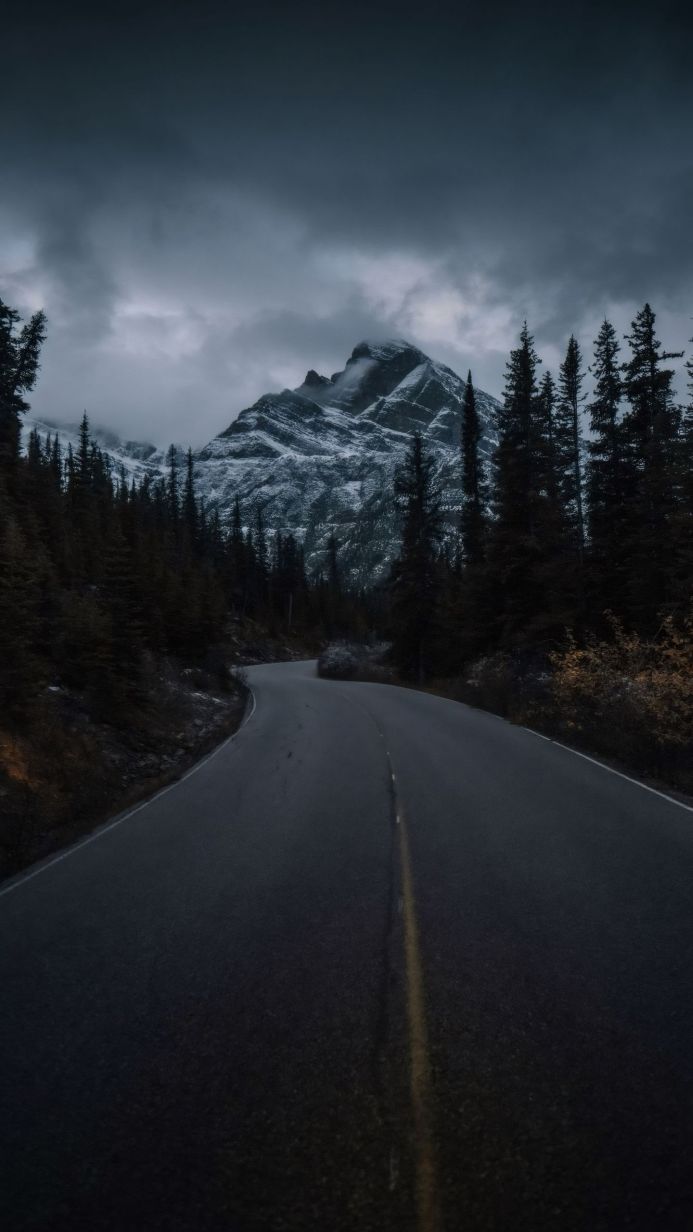 A winding road leading to a snow-capped mountain under a cloudy sky