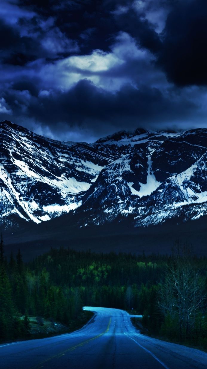 A winding road leads to snow-capped mountains under a cloudy sky