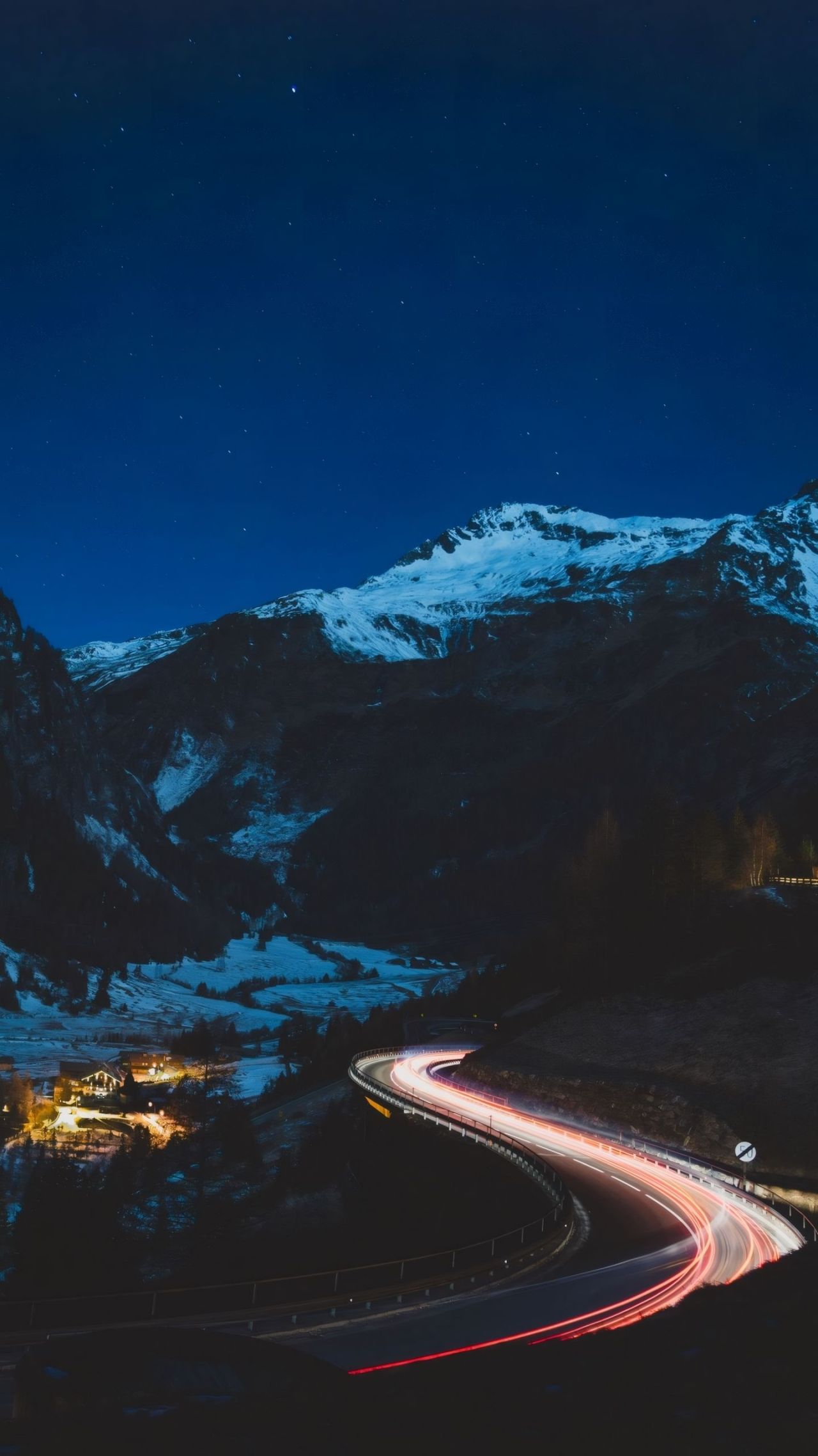 Mountain road at night with light trails and village