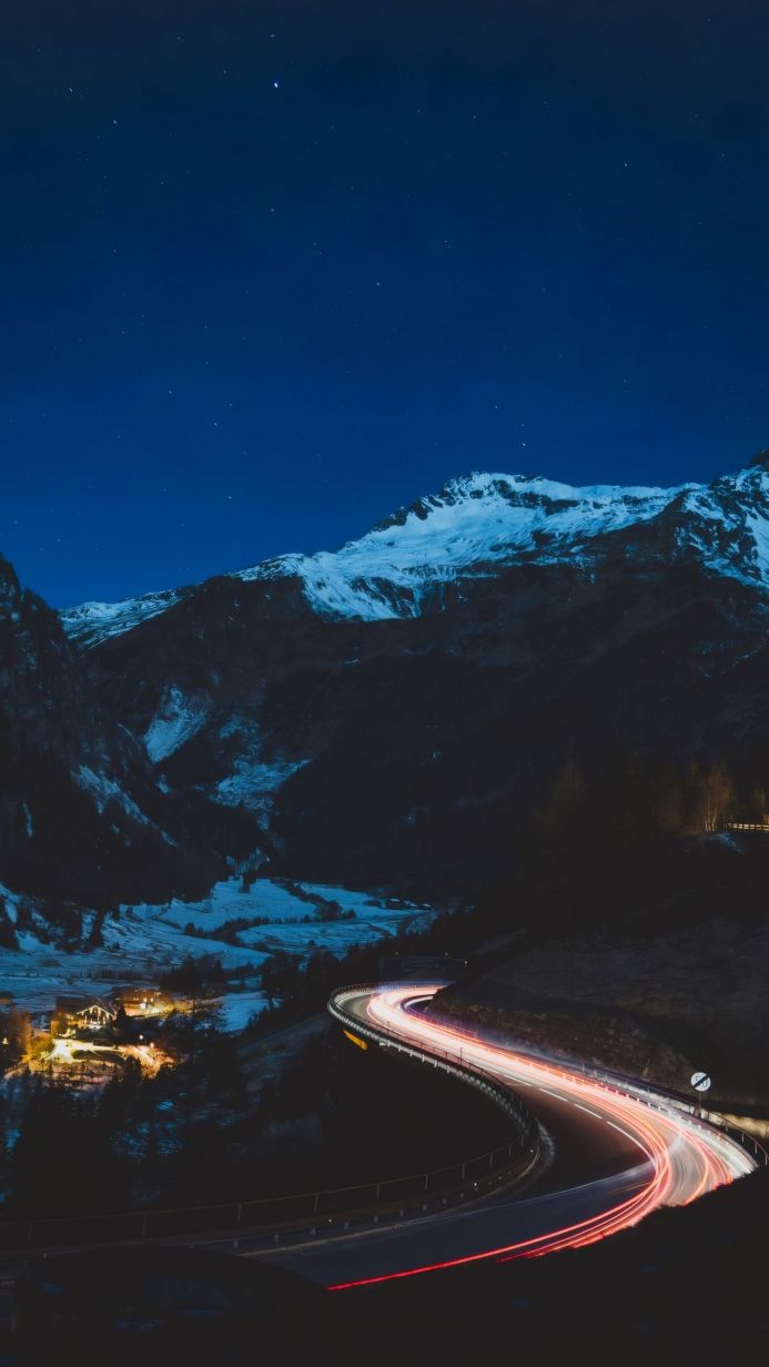 Long exposure shot of car lights on a mountain road at night under a starry sky