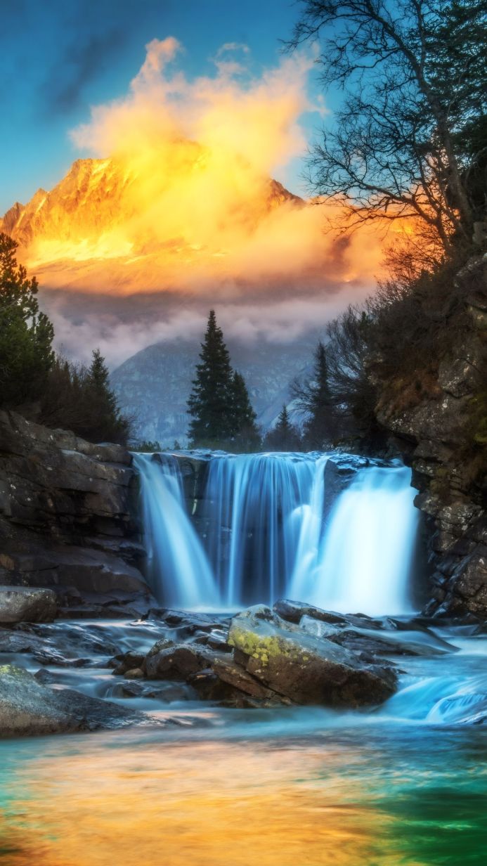 Waterfall cascading into a pool, with a golden mountain partially obscured by clouds in the background