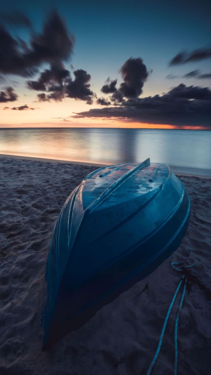 An overturned blue boat on a sandy beach at sunset