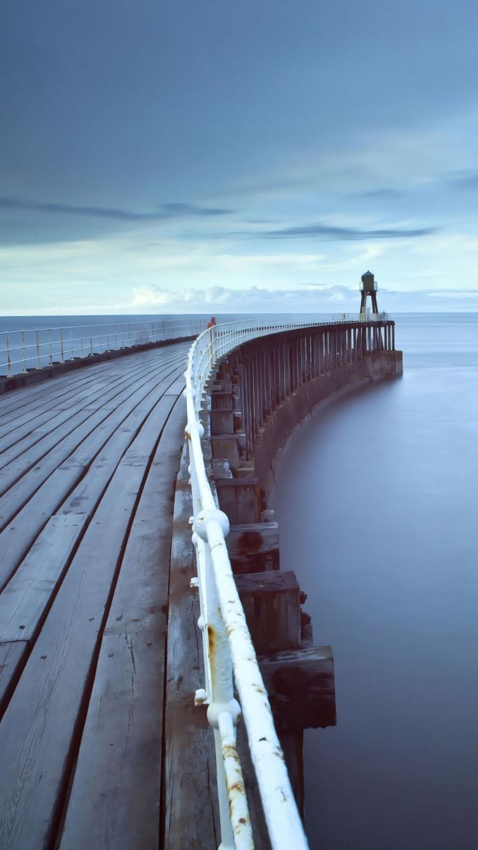 A long pier stretching into the sea under a cloudy sky