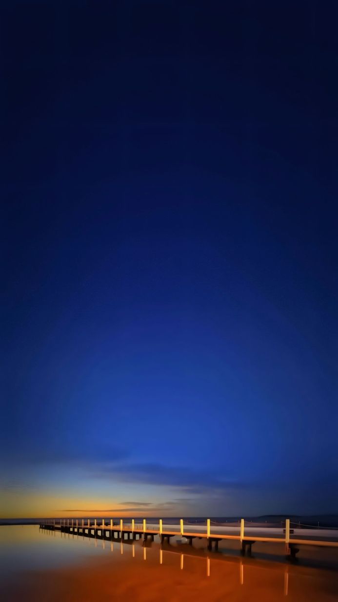 A pier stretching into calm water under a blue sky at dusk