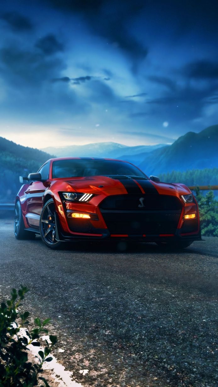 Red Ford Mustang Shelby GT500 with black stripes parked on a road with a mountain backdrop