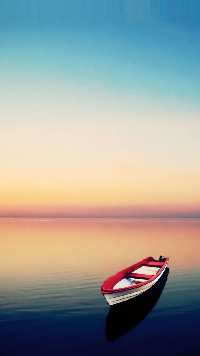 A red and white boat floating on calm water at sunset