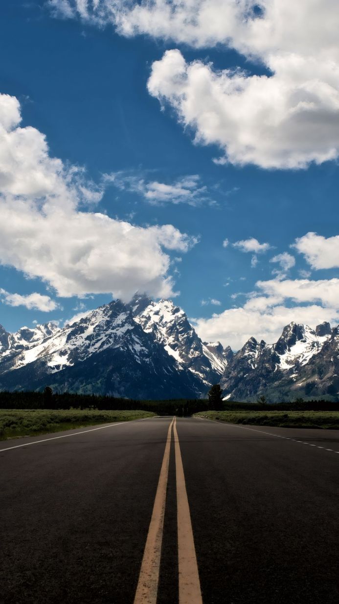 A road leading to snow-capped mountains under a blue sky with white clouds