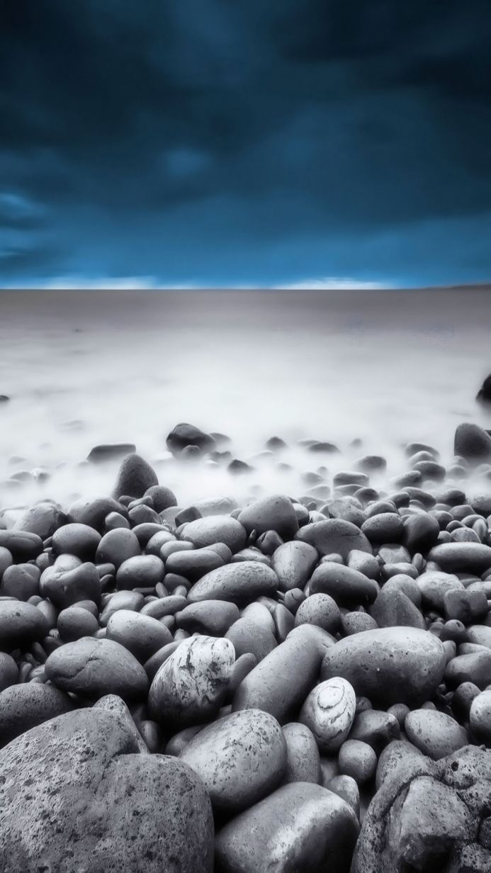 Monochrome image of a rocky beach with a blurred ocean and blue sky