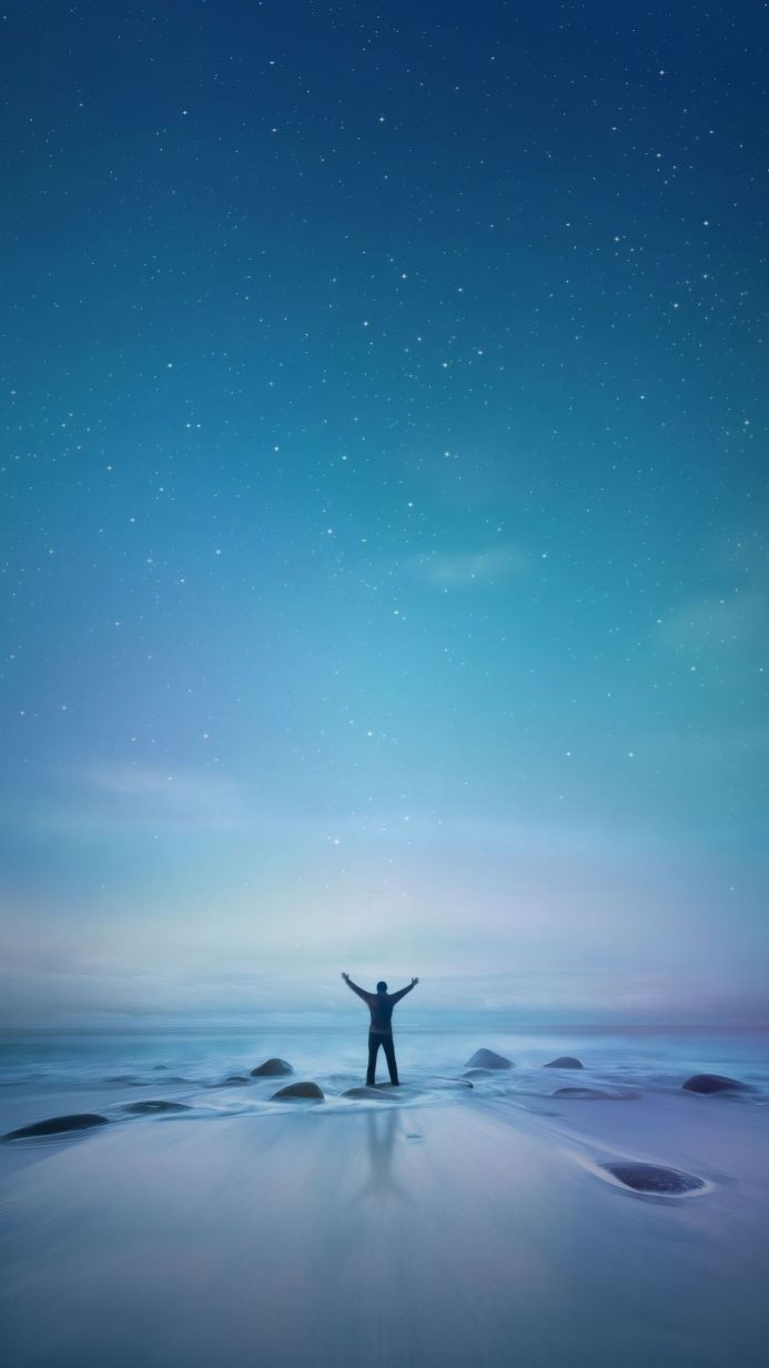 Silhouette on a beach with arms raised towards a starry sky
