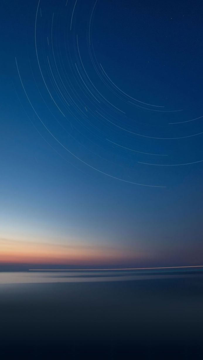 Star trails in a dark blue sky over a calm ocean landscape at sunset