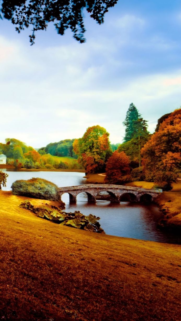 A stone bridge over a lake surrounded by trees in autumn colors