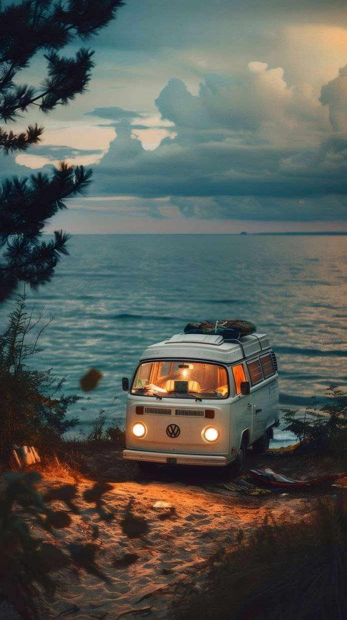 A vintage Volkswagen van parked near the sea at dusk, with a surfboard on top