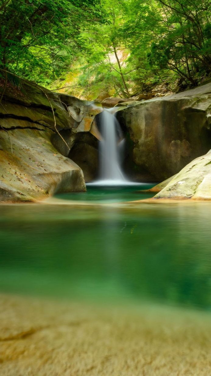 A scenic waterfall flowing into a clear pool surrounded by rocks and lush greenery