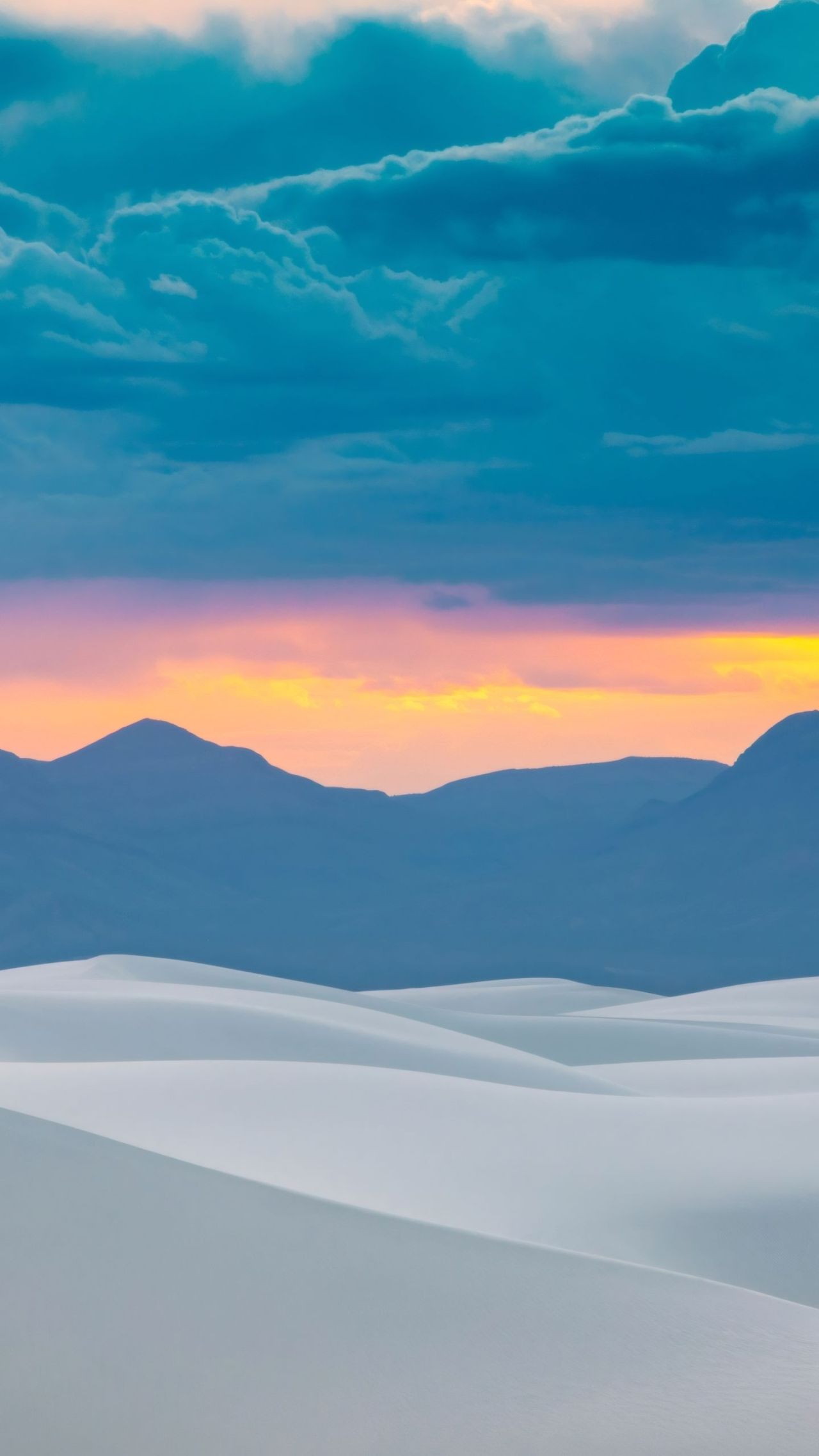 White sand dunes at sunset with mountains and colorful sky