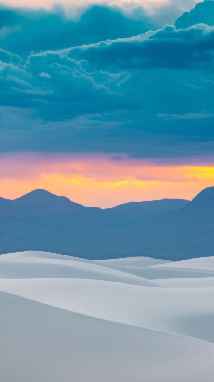 White sand dunes with mountains under a colorful sky