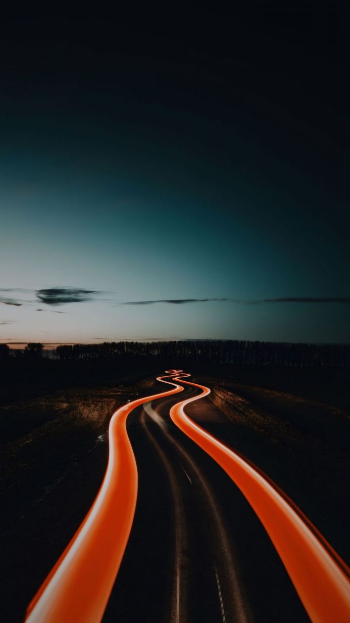 A winding road at night with orange light trails from passing cars
