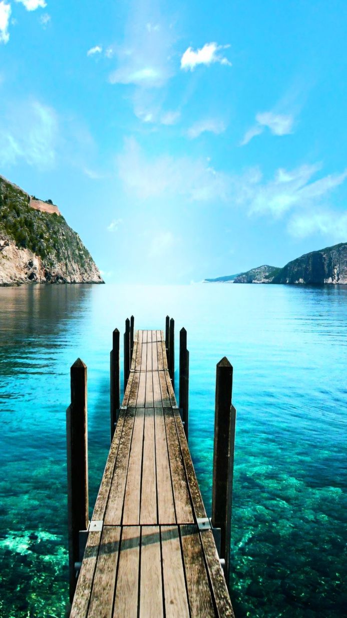 Wooden pier extending into turquoise water with mountains in the background under a clear blue sky