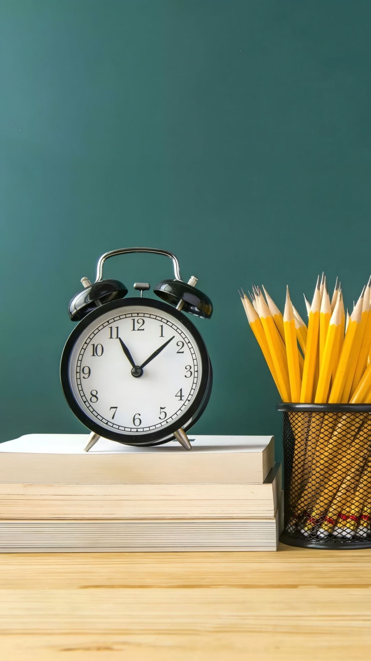 Alarm clock, books, pencils on table with green background