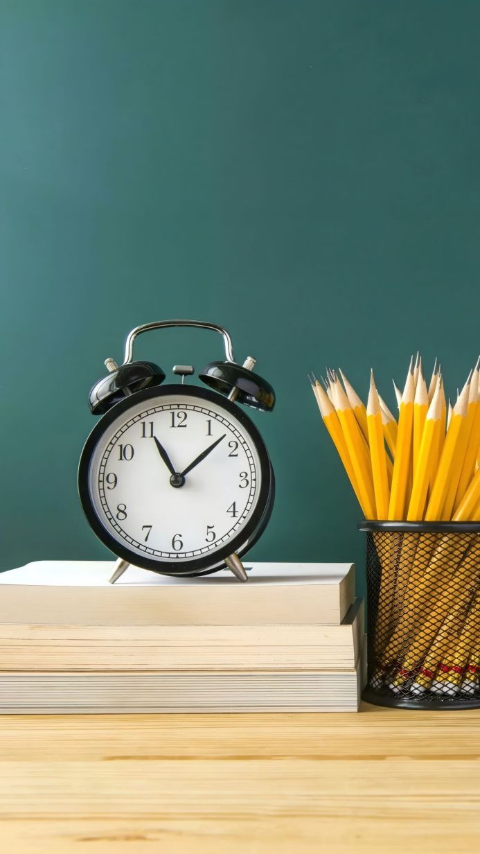 Alarm clock on books with yellow pencils on a green background