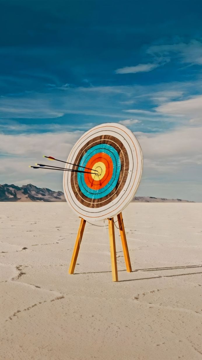 Archery target with three arrows in the bullseye on a salt flat with mountains in the distance