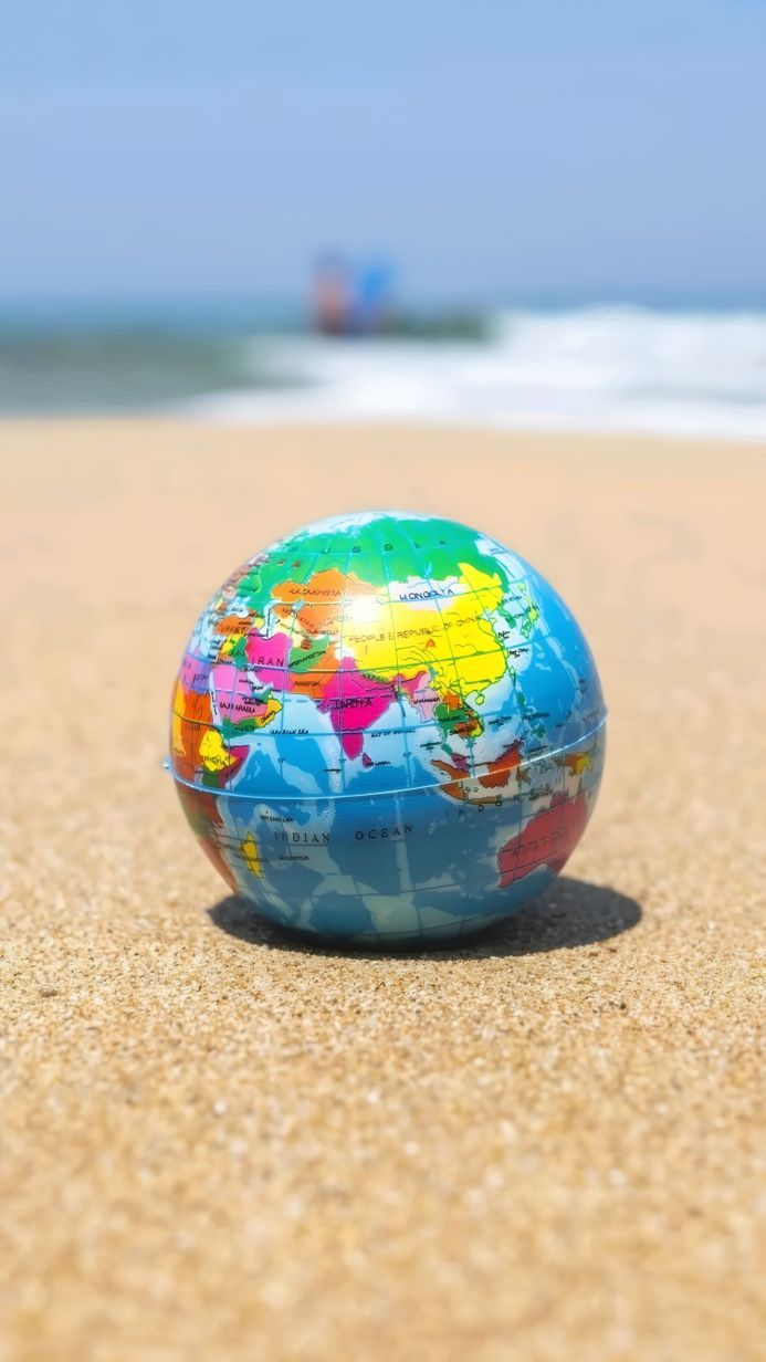 A colorful globe sitting on a sandy beach with the ocean in the background