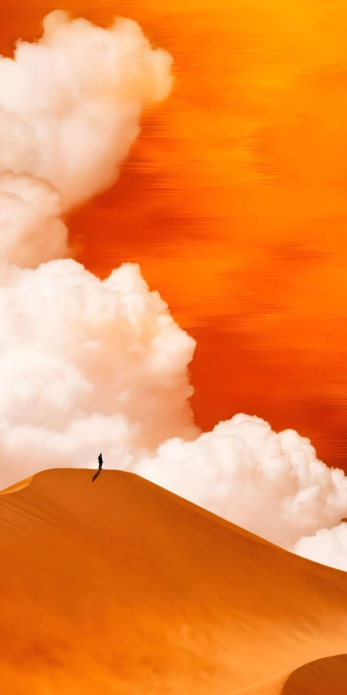 A person stands on top of a sand dune under a cloudy orange sky