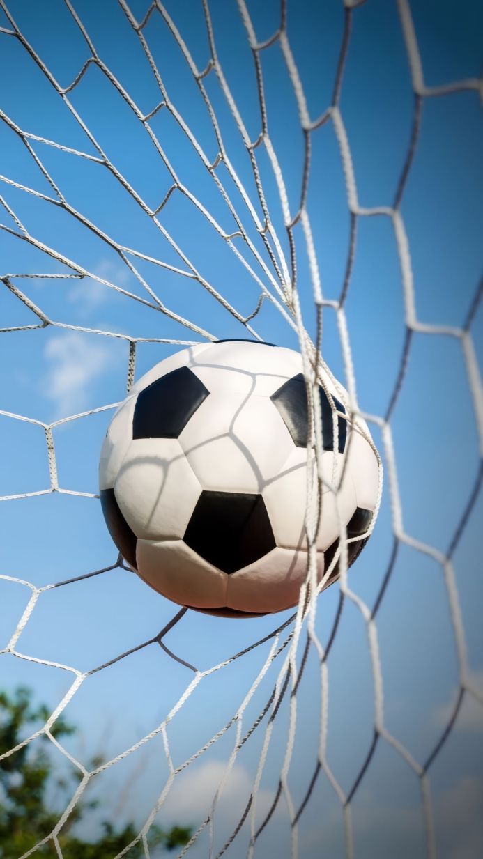A soccer ball hitting the back of a white net with a blue sky background