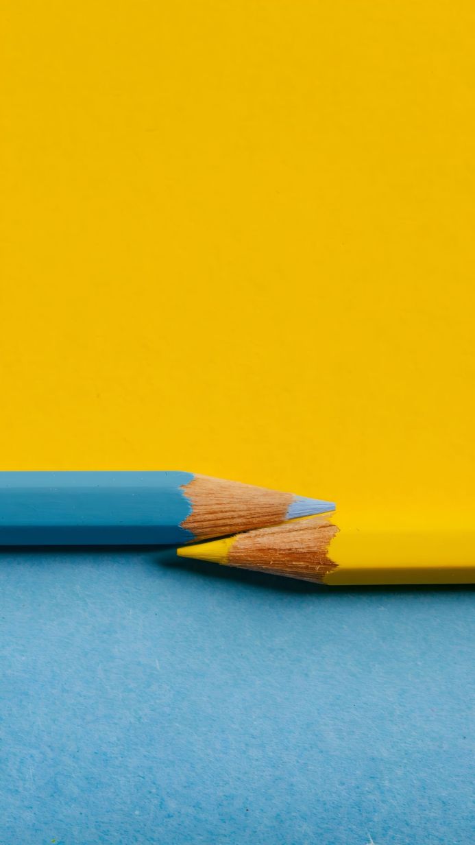 A yellow and blue pencil lying on a blue and yellow background